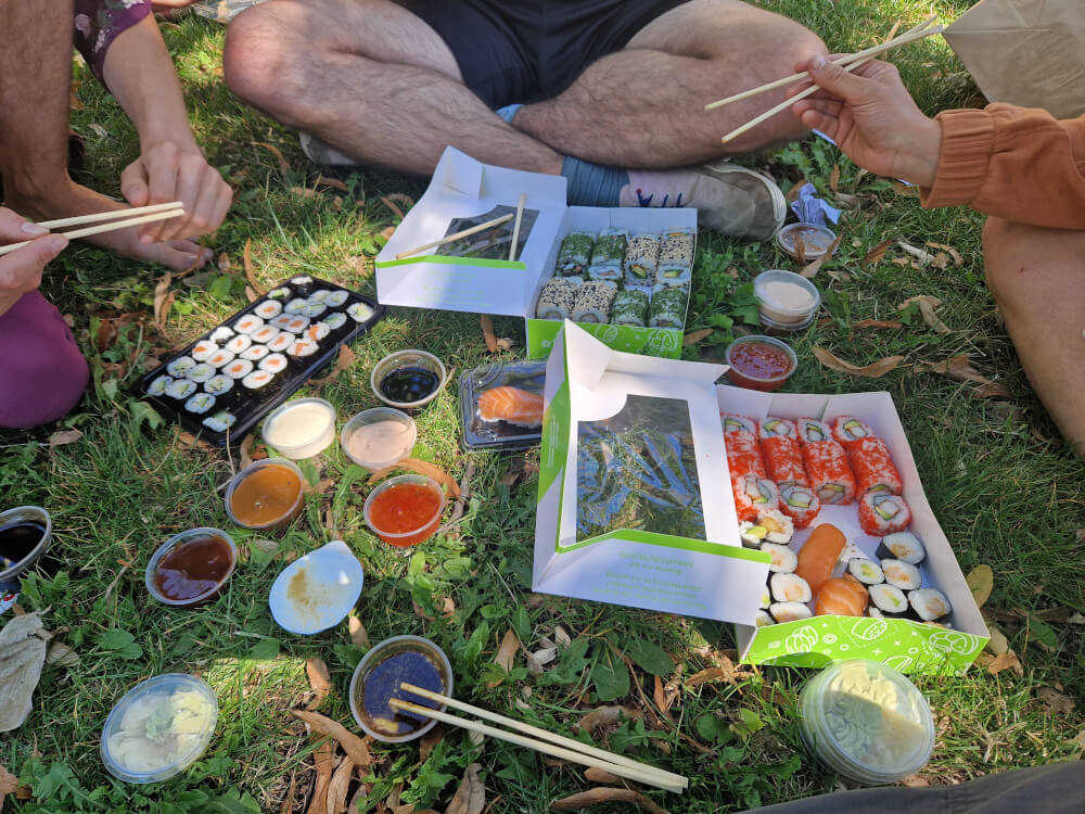 Mehrere Gründungsmitglieder teilen im Park eine große Portion Sushi